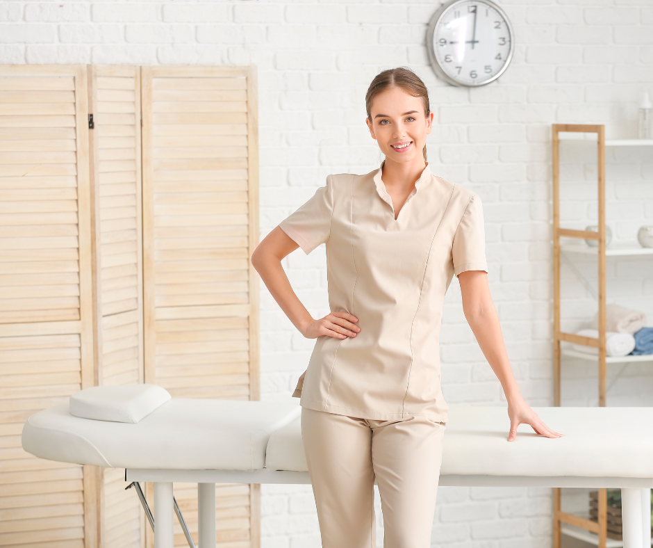 In-home massage therapist smiling pleasantly, standing at a massage table